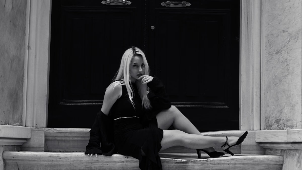 Elegant black and white portrait of a woman in urban fashion sitting on steps.